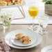 A table with a white Acopa wide rim plate of biscuits and a glass of orange juice.