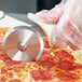 A person using a Dexter-Russell pizza cutter to slice a pizza.