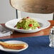 A plate of spaghetti in a white stoneware bowl with tomatoes and cheese on a table.