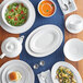 A table set with Acopa bright white rolled edge stoneware plates and bowls with a white bouillon cup filled with orange soup.