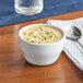 A white bouillon cup of soup with a spoon on a table.