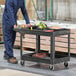 A man in blue overalls uses a Rubbermaid black lipped utility cart to hold tools.