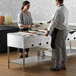 A man and woman standing next to a ServIt electric steam table holding plates of food.