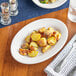 A plate of potatoes on an Acopa Bright White oval platter with a fork and knife.