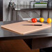 A San Jamar brown cutting board with a knife on a table with tomatoes and oranges.