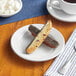 An Acopa Bright White wide rim stoneware plate with a piece of chocolate and a cup of coffee on a table.