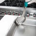 A person holding a Vollrath teal oval Spoodle over a metal tray.