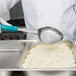 A person in a white uniform using a Vollrath teal metal Spoodle to serve food