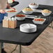 A woman using a white bowl to serve herself rice and beans from a table with a Creative Converting Stay Put Black plastic tablecloth.