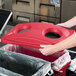 A person putting a red lid on a Rubbermaid Slim Jim recycling container.