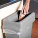 A hand putting a coffee cup into a Rubbermaid Slim Jim trash can.