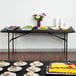 A black rectangular table with food on it and a purple jar of flowers.