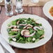 A Tuxton ivory china plate with a salad of spinach, mushrooms, and onions