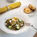 A Tuxton ivory china plate with scalloped edges holding a plate of pasta and a fork.