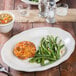 A Tuxton eggshell oval china platter with food on a table.