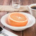 A Tuxton eggshell scalloped edge china grapefruit bowl with half an orange in it on a table next to a cup of coffee.