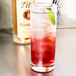 A close-up of an Anchor Hocking Regency Collins glass filled with a red cocktail and ice with a lime garnish.