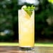 An Anchor Hocking Regency Collins Glass filled with yellow liquid and garnished with mint leaves and an apple slice.