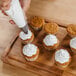 A hand using an Ateco open star piping tip to pipe white frosting on a cupcake.