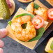 A hand holding a small Tablecraft bamboo square dish with a shrimp on it.