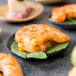 A Tablecraft black bamboo round dish with shrimp and peppers on a table.