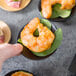 A hand holding a Tablecraft black bamboo dish with shrimp on it.