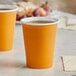 Two yellow Creative Converting Pumpkin Spice paper hot cups filled with coffee on a table.