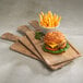 A cheeseburger and a bowl of french fries served on a rectangular faux driftwood serving board with a full pocket and handle.