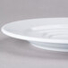 A close-up of a white Elite Global Solutions double well coffee saucer on a gray surface.