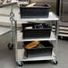 A Lakeside stainless steel utility cart with purple leg bumpers holding black containers.