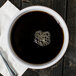 A white melamine cup of coffee with a spoon and napkin.