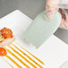 A person's hand using a Mercer Culinary silicone spatula to plate a piece of meat with a tomato.