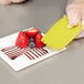 A person using a yellow Mercer Culinary silicone spatula to plate strawberries.