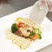 A white plate with broccoli and tomato slices on it, with a Mercer Culinary silicone plating tool.