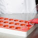 A person pouring red liquid into a red Martellato round silicone candy mold.