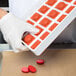 A gloved hand holding a Martellato red silicone round mold tray with red circles.