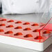 A person pouring red liquid into a red and white heart shaped silicone mold.