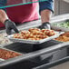 A person in black gloves holding a Choice stainless steel steam table pan of food.