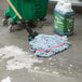 A Rubbermaid blue blend wet mop head on a green bucket of soapy liquid.