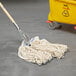 A Rubbermaid white cotton wet mop with a yellow handle in a yellow bucket.