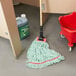 A green Rubbermaid mop head on the floor next to a red bucket.