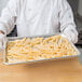 A person holding a Choice aluminum perforated bun pan filled with french fries.