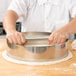 A person using an American Metalcraft stainless steel dough cutting ring to cut dough in a metal bowl.