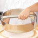 A person using an American Metalcraft stainless steel dough cutting ring to cut dough over a metal bowl.