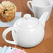 A white Libbey Royal Rideau porcelain teapot on a table with a cup of tea.