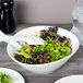 A Libbey round white porcelain bowl filled with salad on a table.