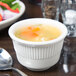 A Tuxton Hampshire eggshell embossed china bouillon cup filled with soup on a table with a spoon