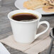 A Libbey tall white porcelain tea cup on a napkin next to a plate of cookies.