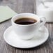 A cup of coffee on a Libbey Royal Rideau white porcelain saucer.