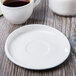 A white Libbey porcelain saucer on a wood surface with a cup of coffee.